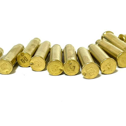 Close-up of empty brass cartridge cases with visible headstamps including letters H, C, and R on a white background.