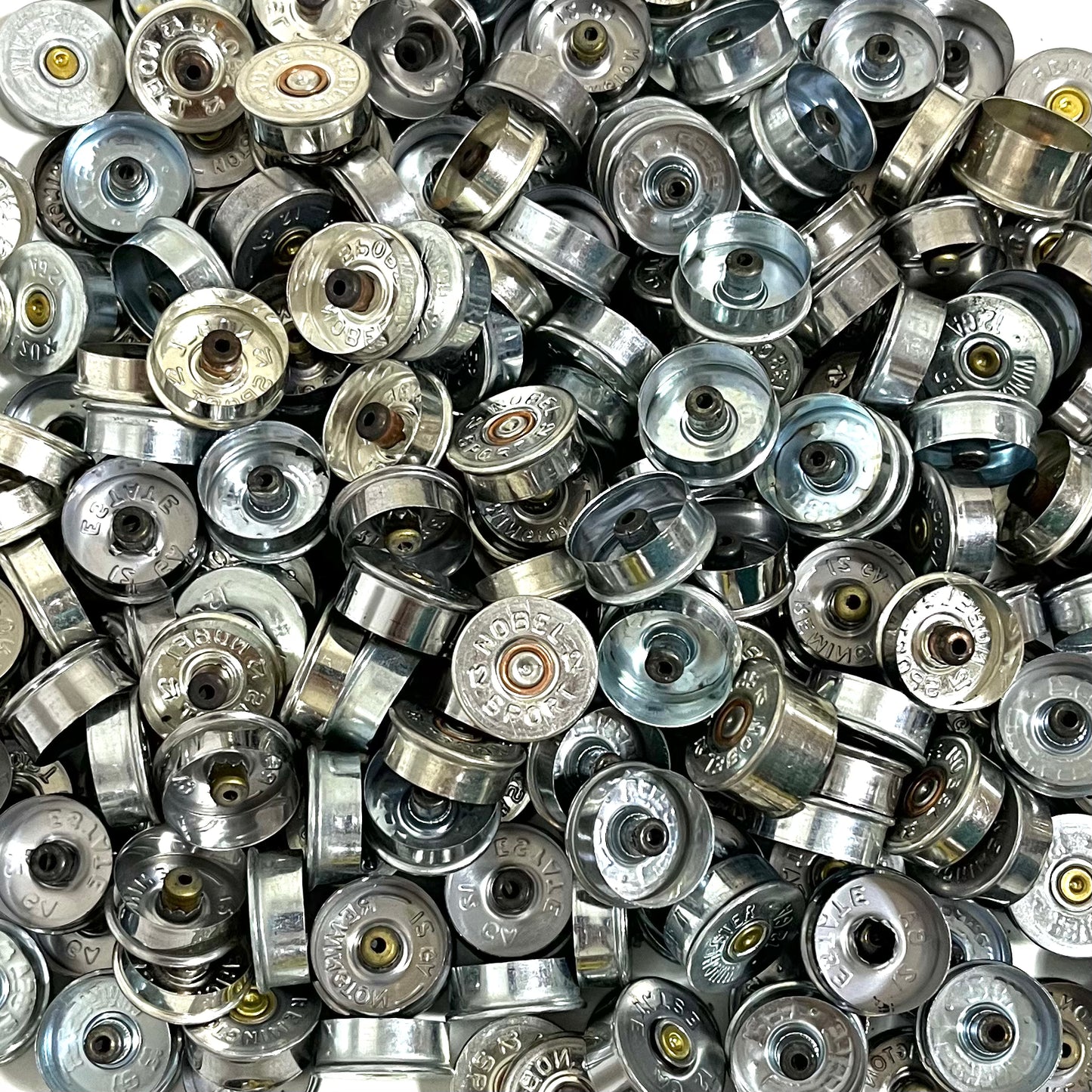 Silver 12 gauge shotgun shell end caps packed together, some showing stamped faces and others interiors.