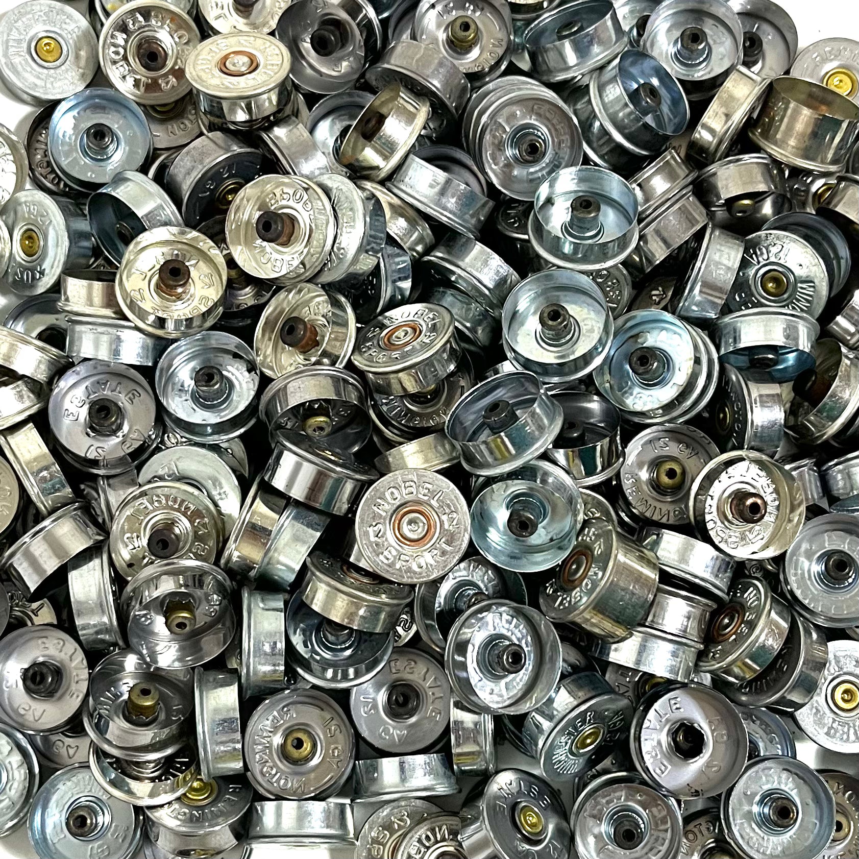 Silver 12 gauge shotgun shell end caps packed together, some showing stamped faces and others interiors.