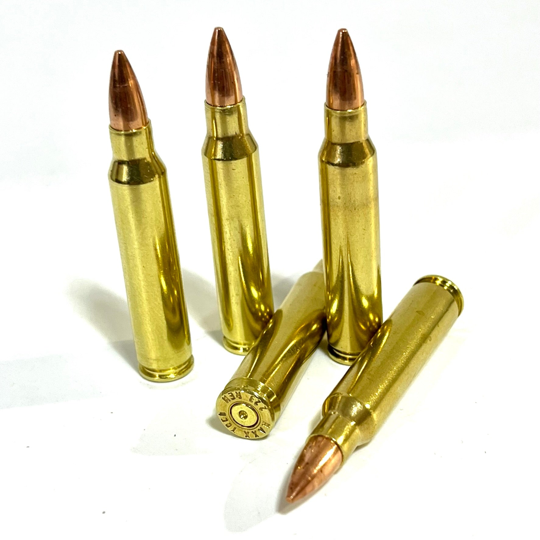 Five brass fake 5.56 dummy cartridges, with three standing upright and two lying down to display the spent primer and headstamp.