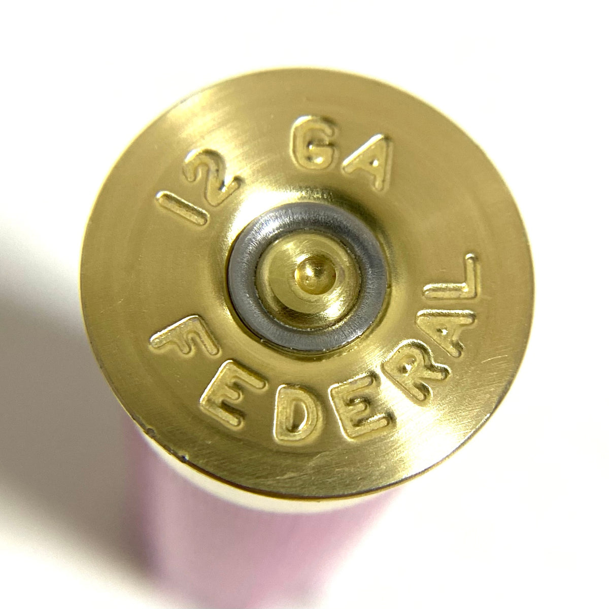 Extreme close-up of a single once-fired pink 12-gauge Federal hull headstamp, showing the spent primer and stamped text.