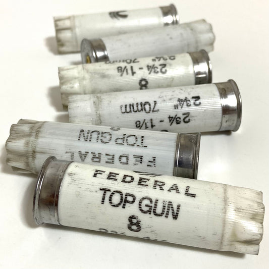 Six used white Federal Top Gun 12ga shells fanned diagonally, showing silver caps