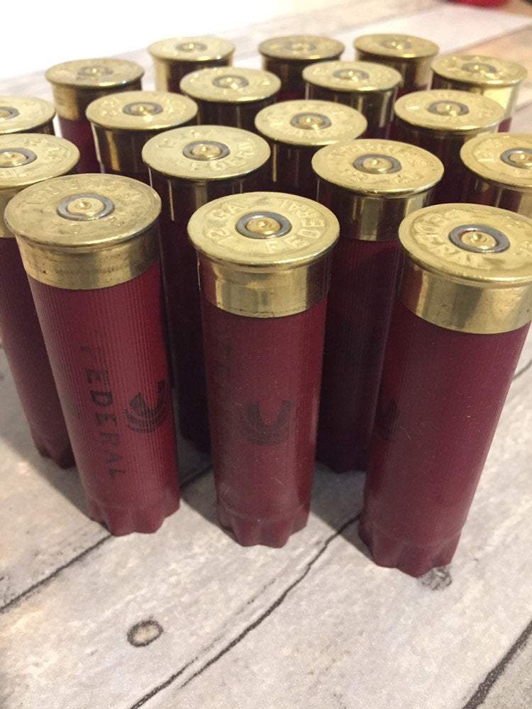 A group of empty dark red Federal 12 gauge shotgun hulls standing upright, showing their brass bases from a high angle.