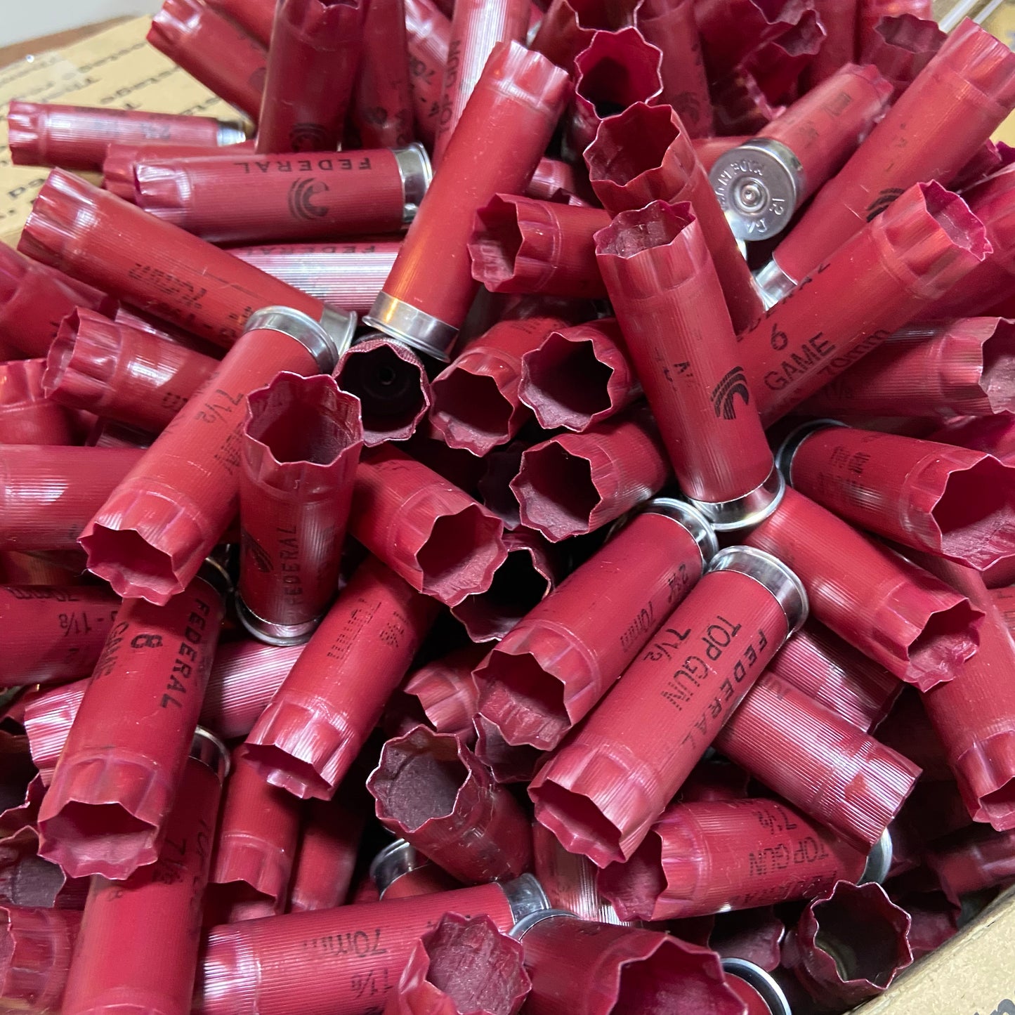 A pile of loose empty dark red shotgun shells of various brands including Federal Top Gun.