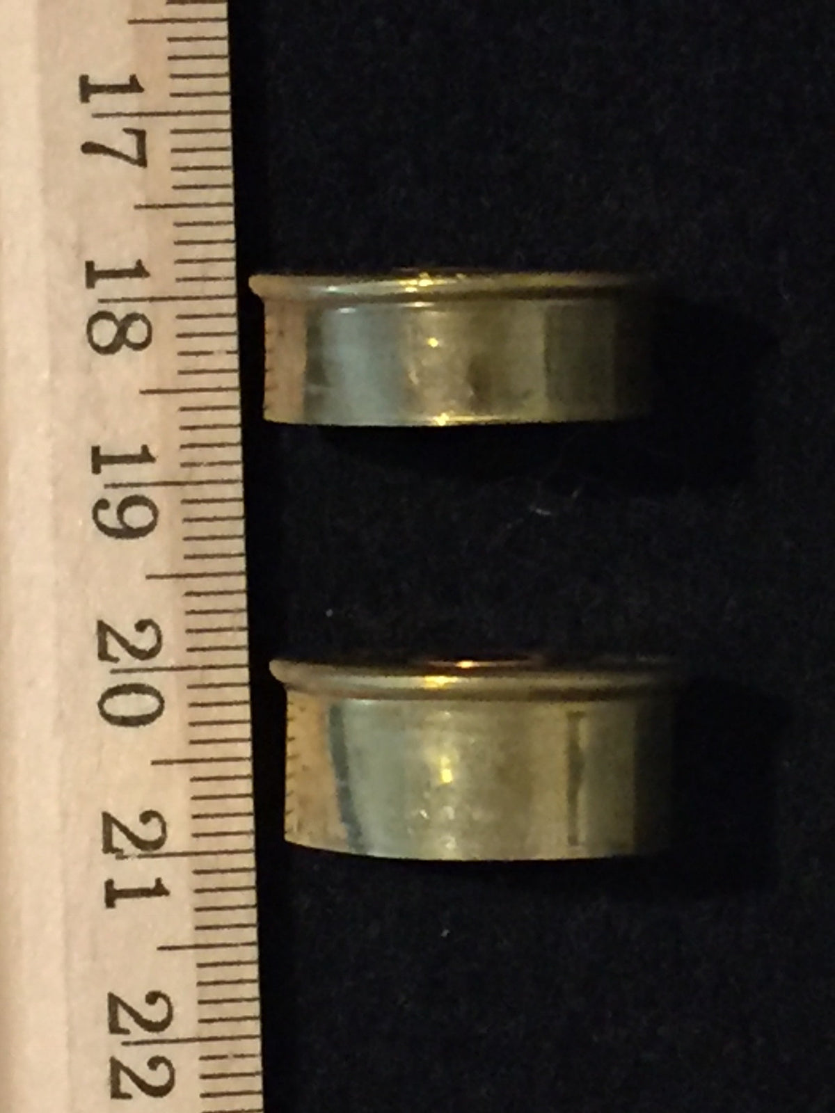 Two gold brass end caps lying flat next to a wooden ruler for size comparison