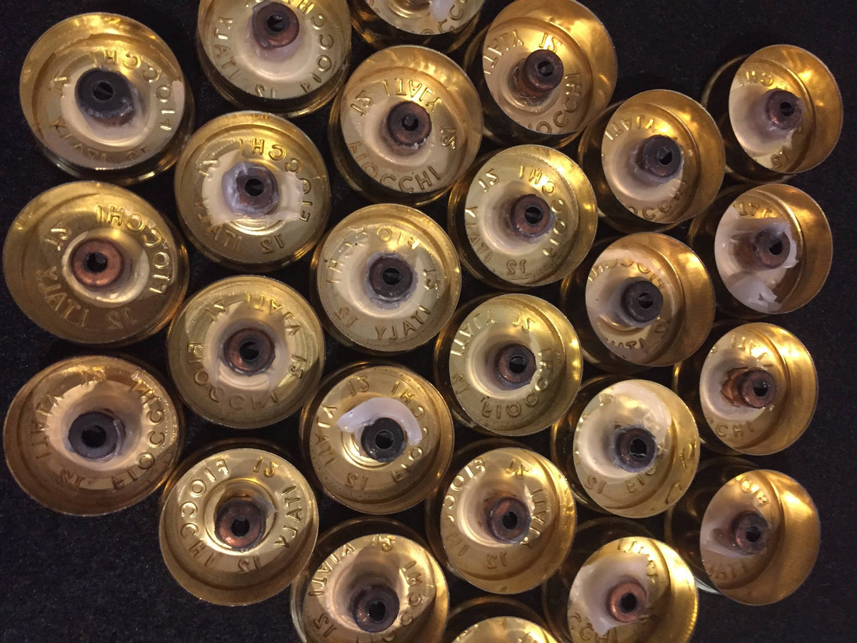 Gold brass headstamps with white residue inside, arranged in overlapping rows on a black surface