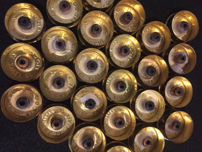 Gold brass headstamps with white residue inside, arranged in overlapping rows on a black surface