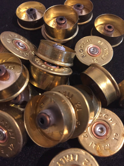 Gold brass Fiocchi 12 gauge headstamps in a pile, some upright and some upside down on a black surface