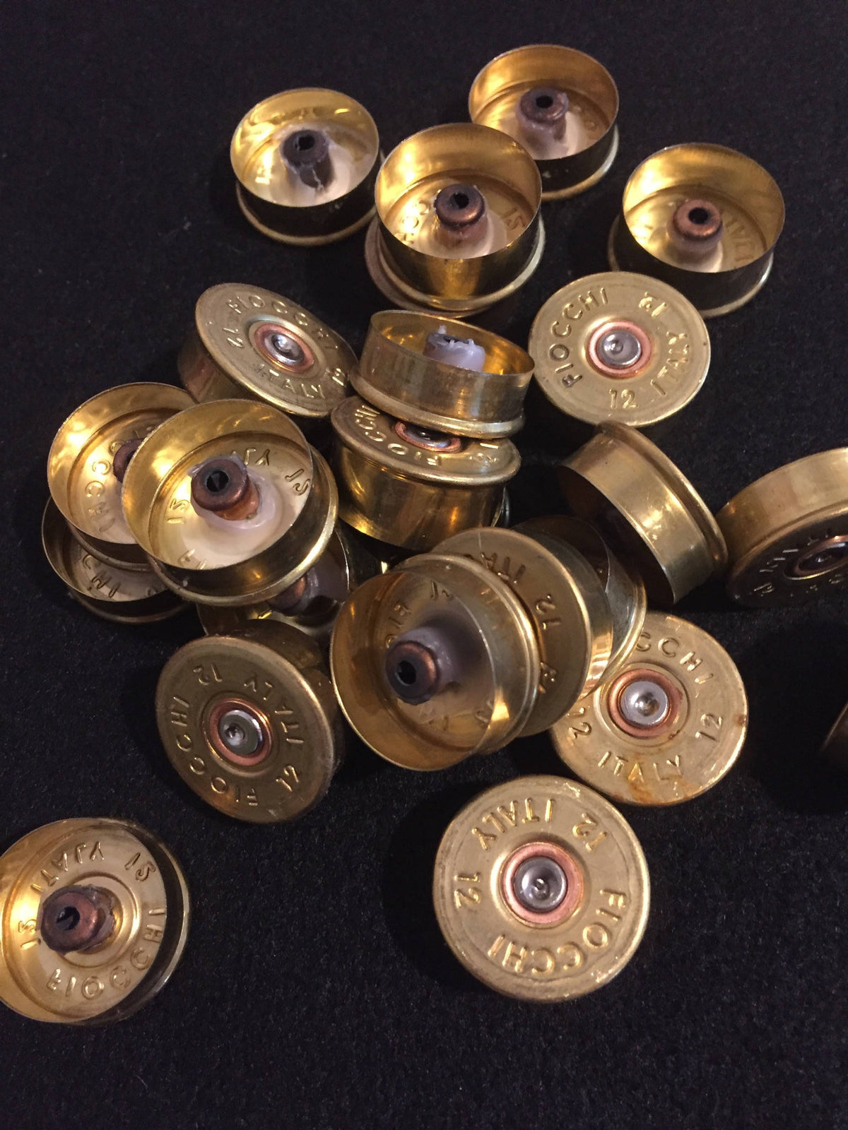 Pile of gold brass Fiocchi 12 gauge headstamps on a black surface