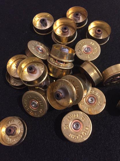 Pile of gold brass Fiocchi 12 gauge headstamps on a black surface