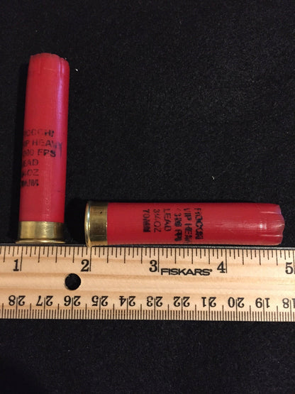 Two red Fiocchi 28 gauge shotgun shell hulls beside a wooden ruler, one marked 70mm on the hull
