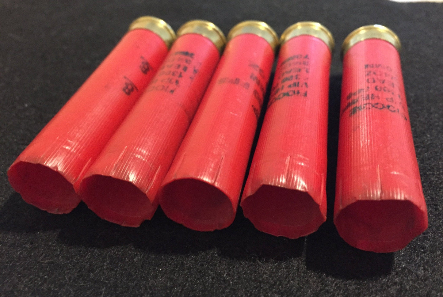 Five red Fiocchi 28 gauge shotgun shell hulls on a dark background showing printed hull markings