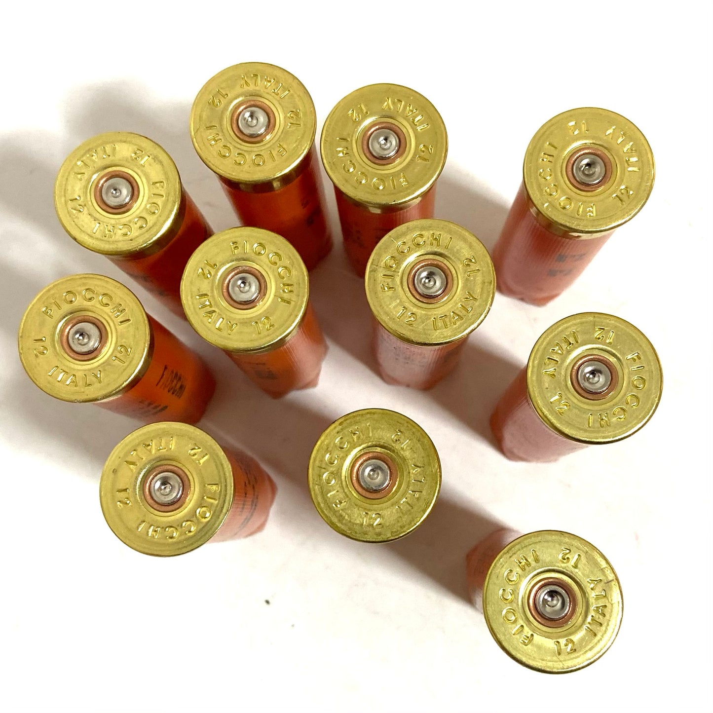 Ten orange Fiocchi 12 gauge hulls viewed from above, showing gold headstamps and fired primers.