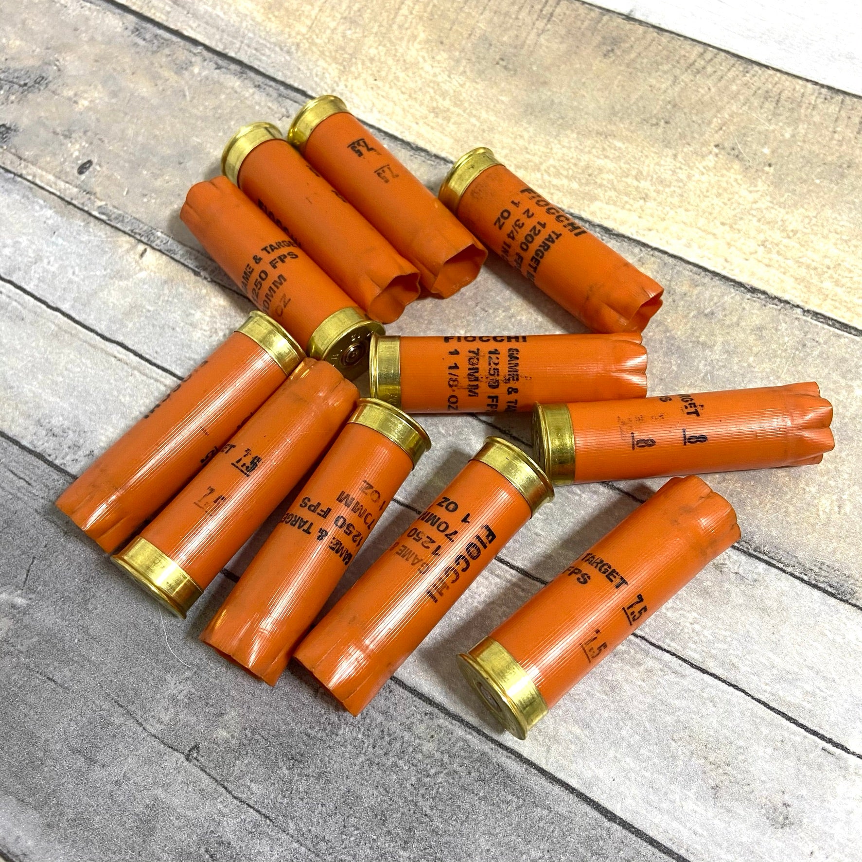 Ten orange Fiocchi shotgun shells arranged in a pinwheel pattern on a rustic wood plank surface.