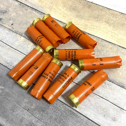 Ten orange Fiocchi shotgun shells arranged in a pinwheel pattern on a rustic wood plank surface.