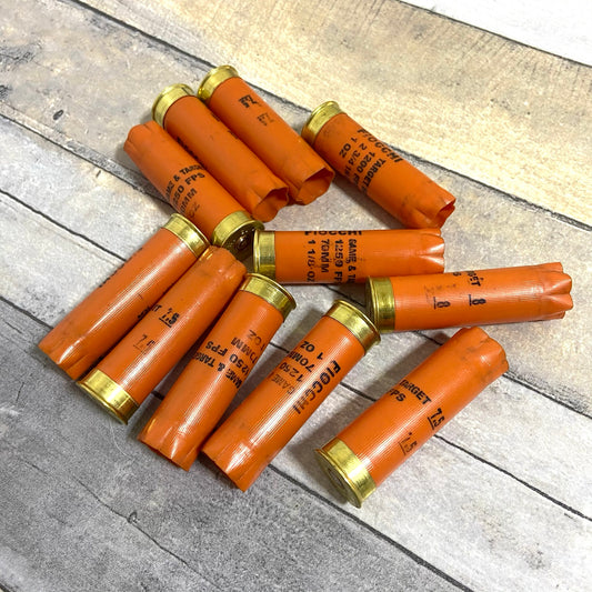 Ten orange Fiocchi shotgun shells arranged in a pinwheel pattern on a rustic wood plank surface.