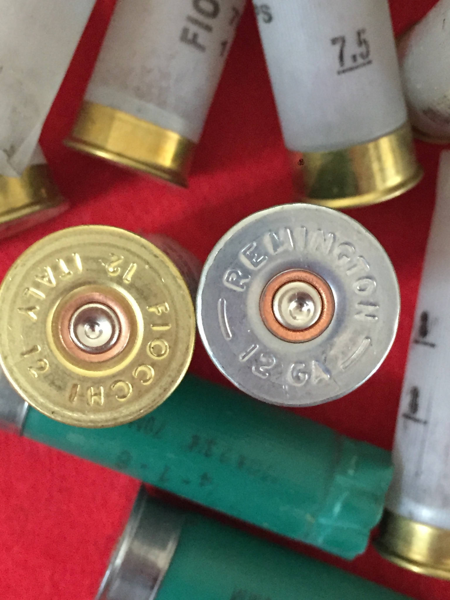 Brass Fiocchi 12 gauge headstamp beside a silver Remington 12 gauge headstamp, close up