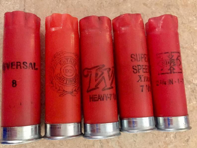 Five red 12 gauge shotgun casings with silver bases standing side-by-side in a row on a tan countertop.