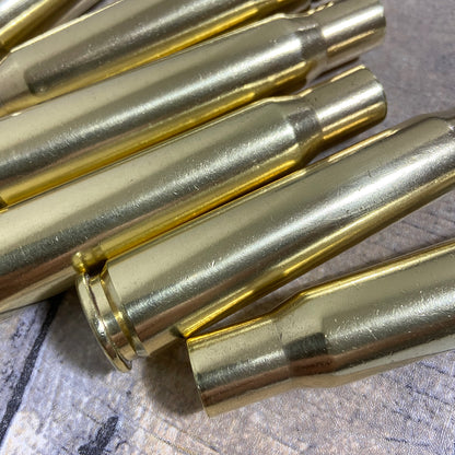 Several hand-polished, genuine once-fired .50 caliber BMG brass casings resting diagonally on a textured gray fabric.