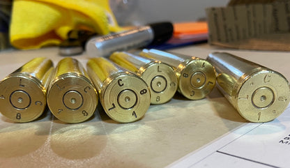 Six empty gold brass casings stand in a row, their headstamps stamped 'LC' visible on each base.