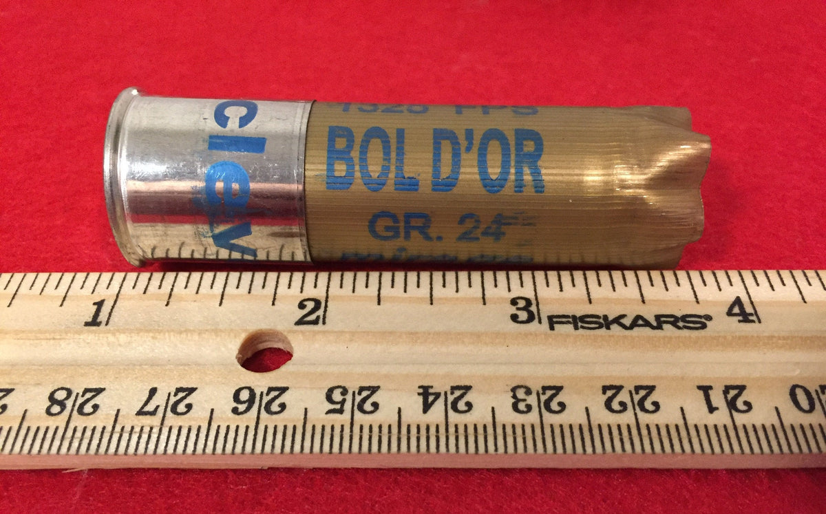 Single gold shotgun shell with a silver base printed "Bol D'Or", "GR.24" next to a ruler on red fabric