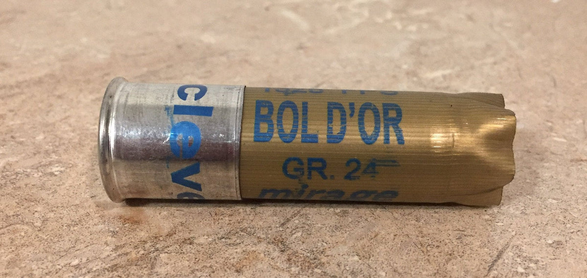Single gold shotgun shell with a silver base printed "Bol D'Or", "GR.24", "mirage" lying on a stone surface