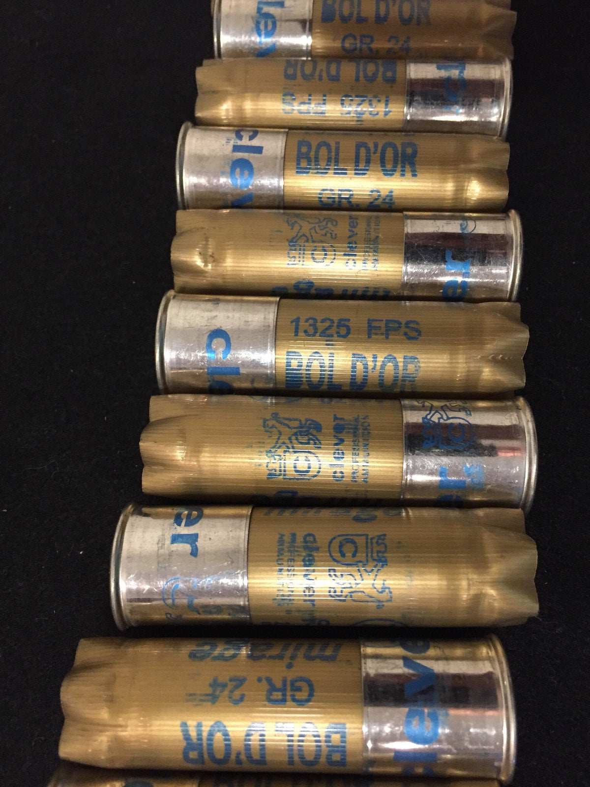 Gold shotgun shells with silver bases lying in a row printed "Bol D'Or", "GR.24", "1325 FPS", "clever" on a black background