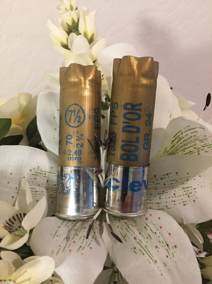2 gold shotgun shells with silver bases standing upright printed "7½", "Bol D'Or", "1325 FPS", "GR.24" among white flowers