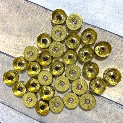 Large pile of gold Fiocchi 12 gauge brass end caps with drilled centers on a wood surface
