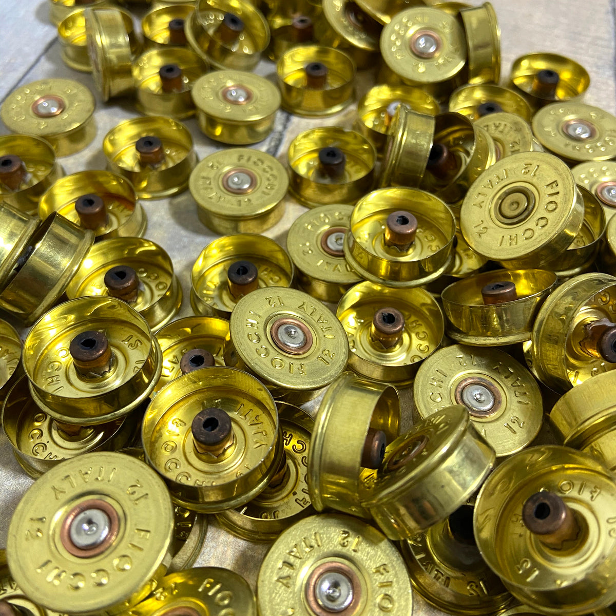 Close-up pile of gold Fiocchi 12 gauge brass end caps showing drilled centers on a wood surface