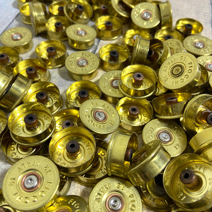 Close-up pile of gold Fiocchi 12 gauge brass end caps showing drilled centers on a wood surface