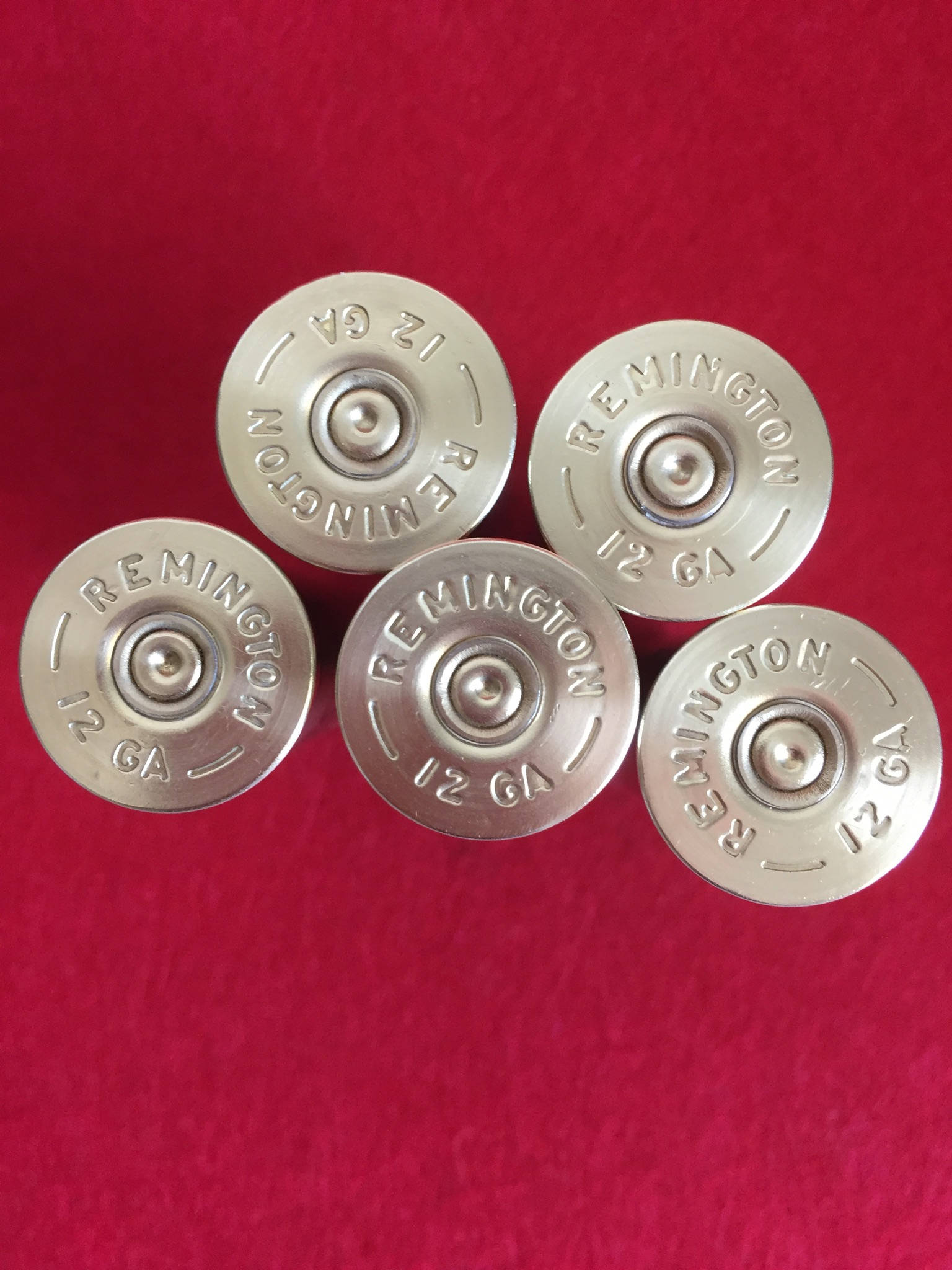 5 silver brass heads of Remington 12 gauge shotgun shells viewed from above on a red surface