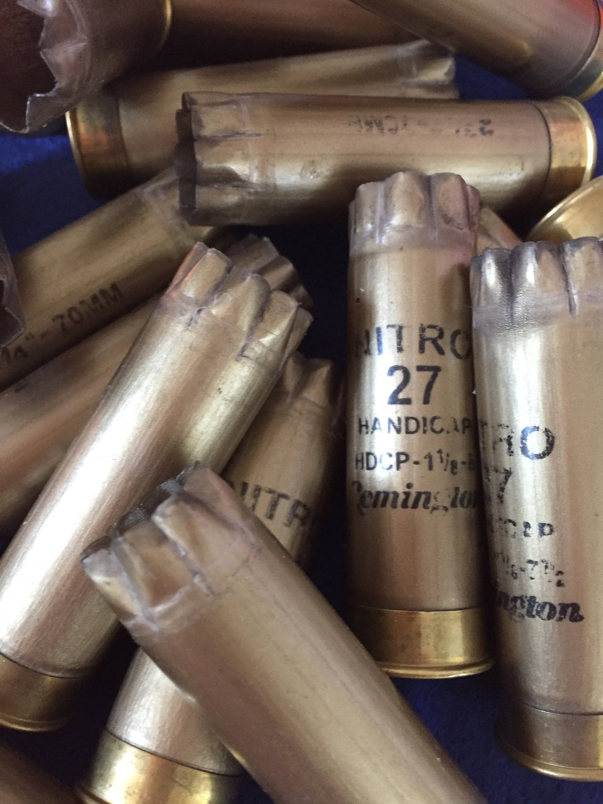 Closeup of gold Remington Nitro shotgun shells piled together, showing star-crimped tops and printed “Nitro 27” markings