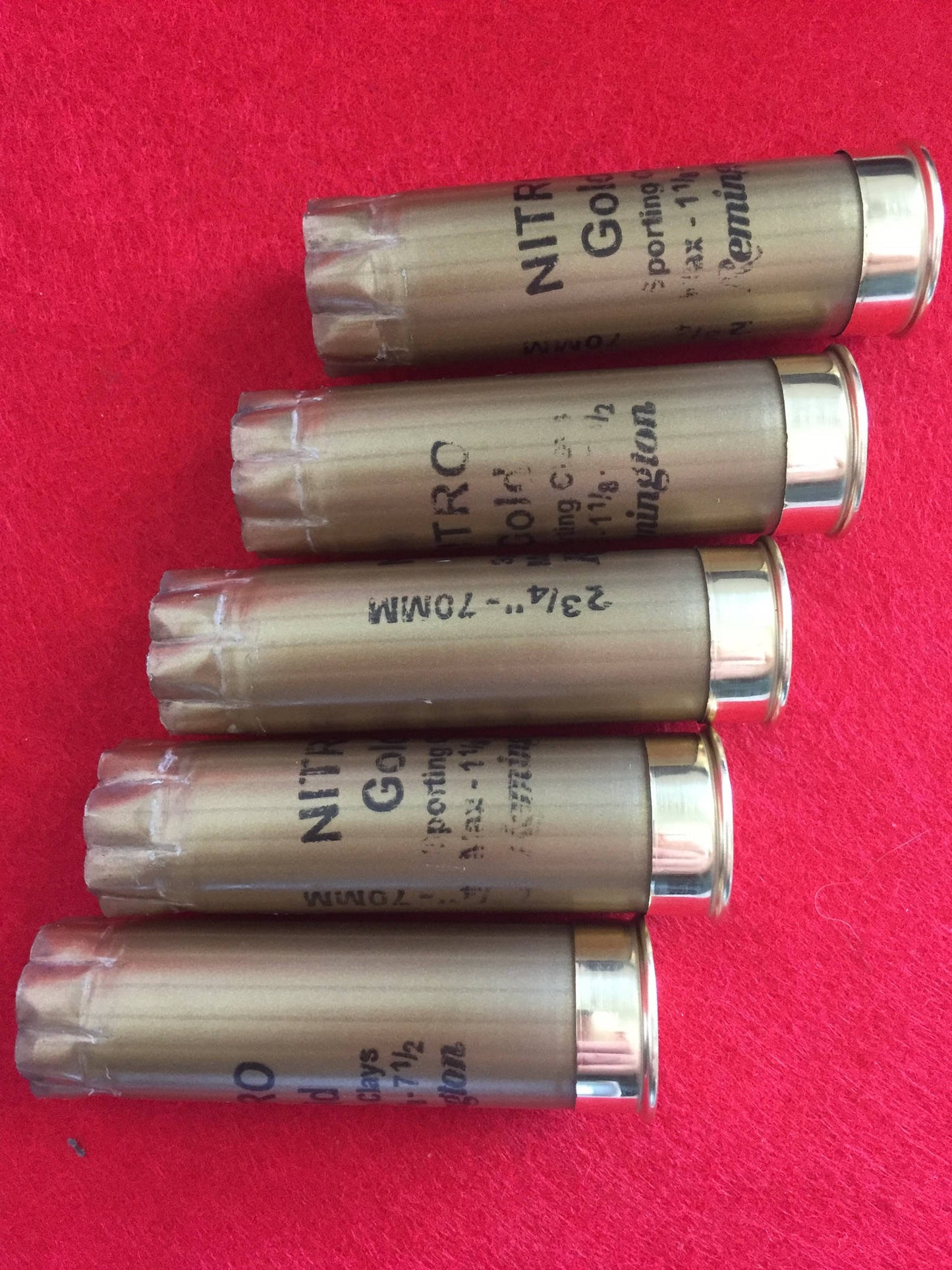 5 gold Remington Nitro shotgun shells lying diagonally on a red surface showing printed text