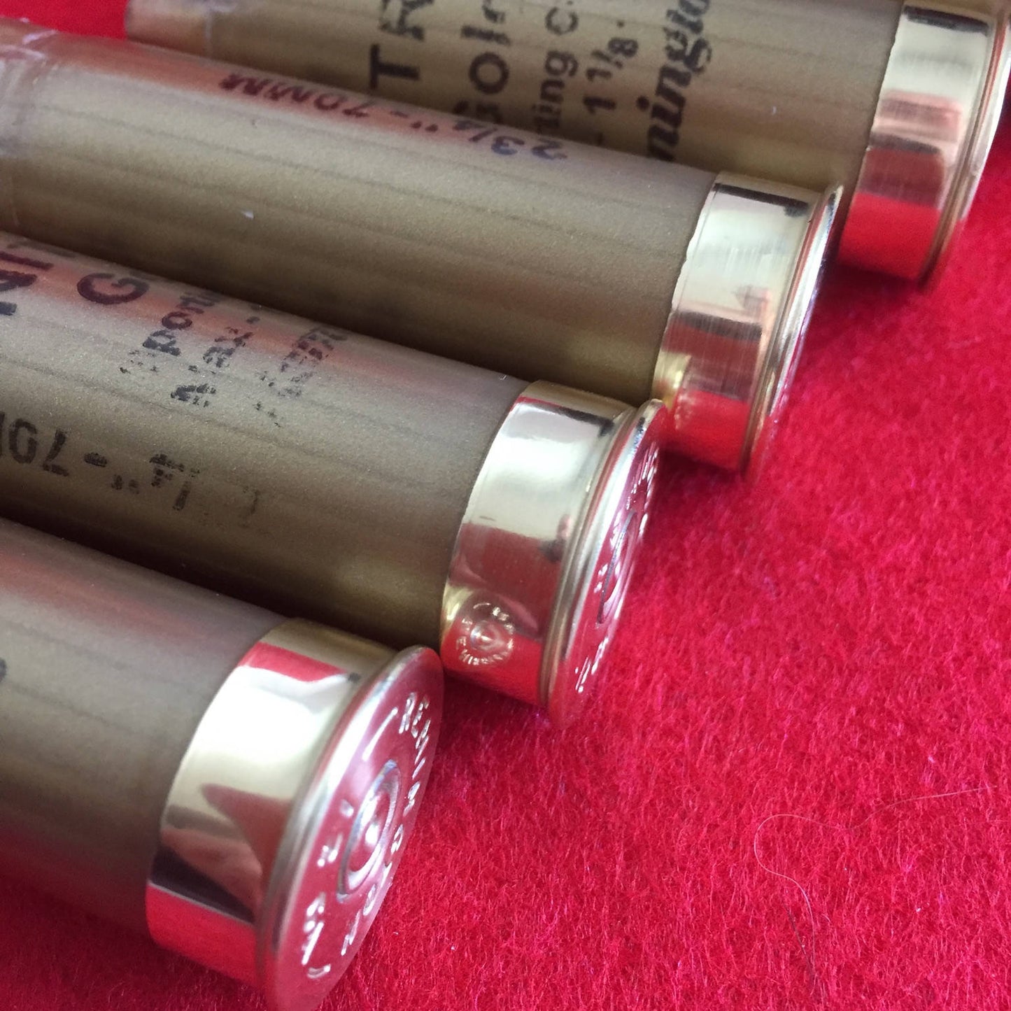 Gold Remington Nitro shotgun shells lying in a row on a red surface showing brass heads and printed text