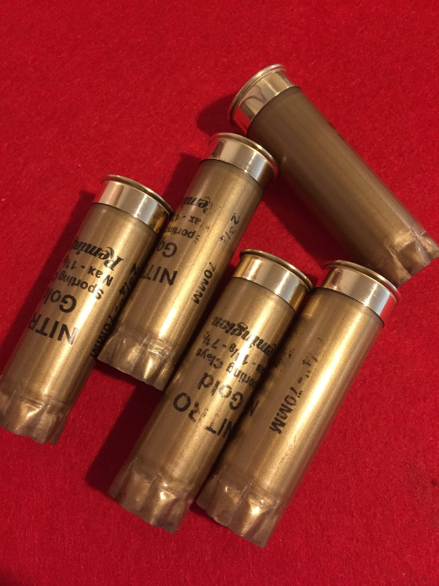 5 gold Remington Nitro 12 gauge shotgun shells lying together on a red surface