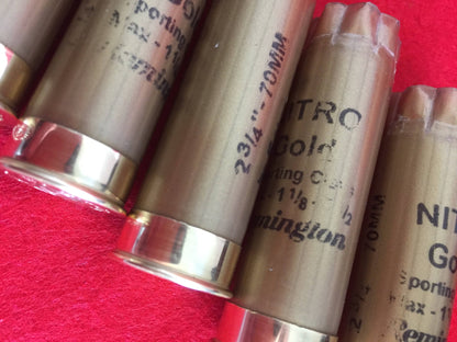 Close-up of gold Remington Nitro shotgun shells showing printed text and brass heads on a red surface