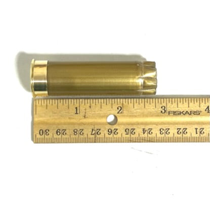 Single gold 12 gauge shotgun hull laid beside a wooden ruler on white, measuring approximately 2.75 inches long.