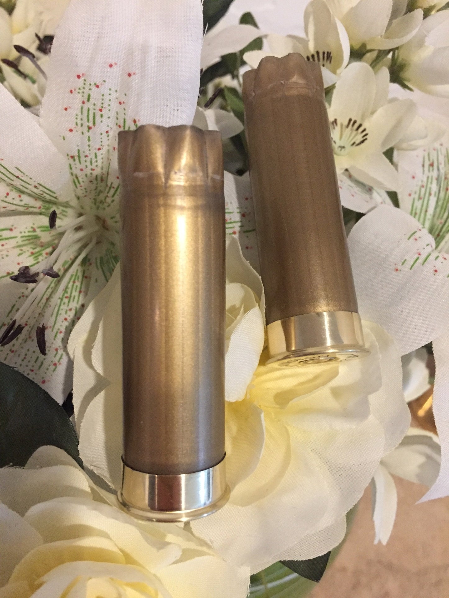 Two gold 12 gauge shotgun hulls standing vertically among white floral wedding boutonnieres.