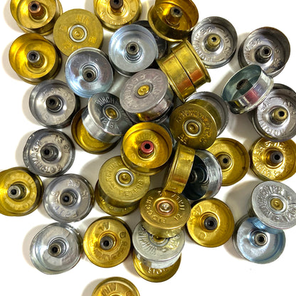 A collection of gold and silver 12 gauge shotgun shell headstamps with empty spent primers.

