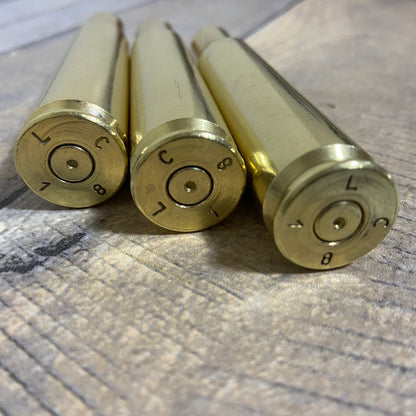 Three spent 50 BMG gold brass cartridges rest base-up on fabric, headstamps stamped 'LC' clearly visible.