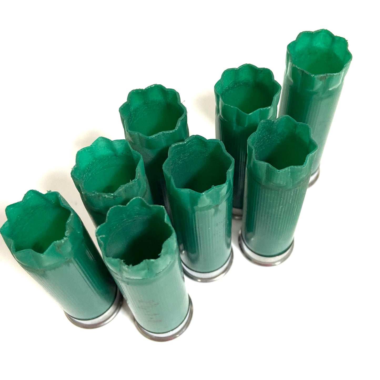 Seven empty green 12ga Remington Gun Club hulls with open star-crimped tops arranged at staggered heights