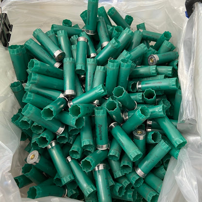 Overhead view of a large bulk pile of spent green 12ga Remington Gun Club cartridges in a plastic bag