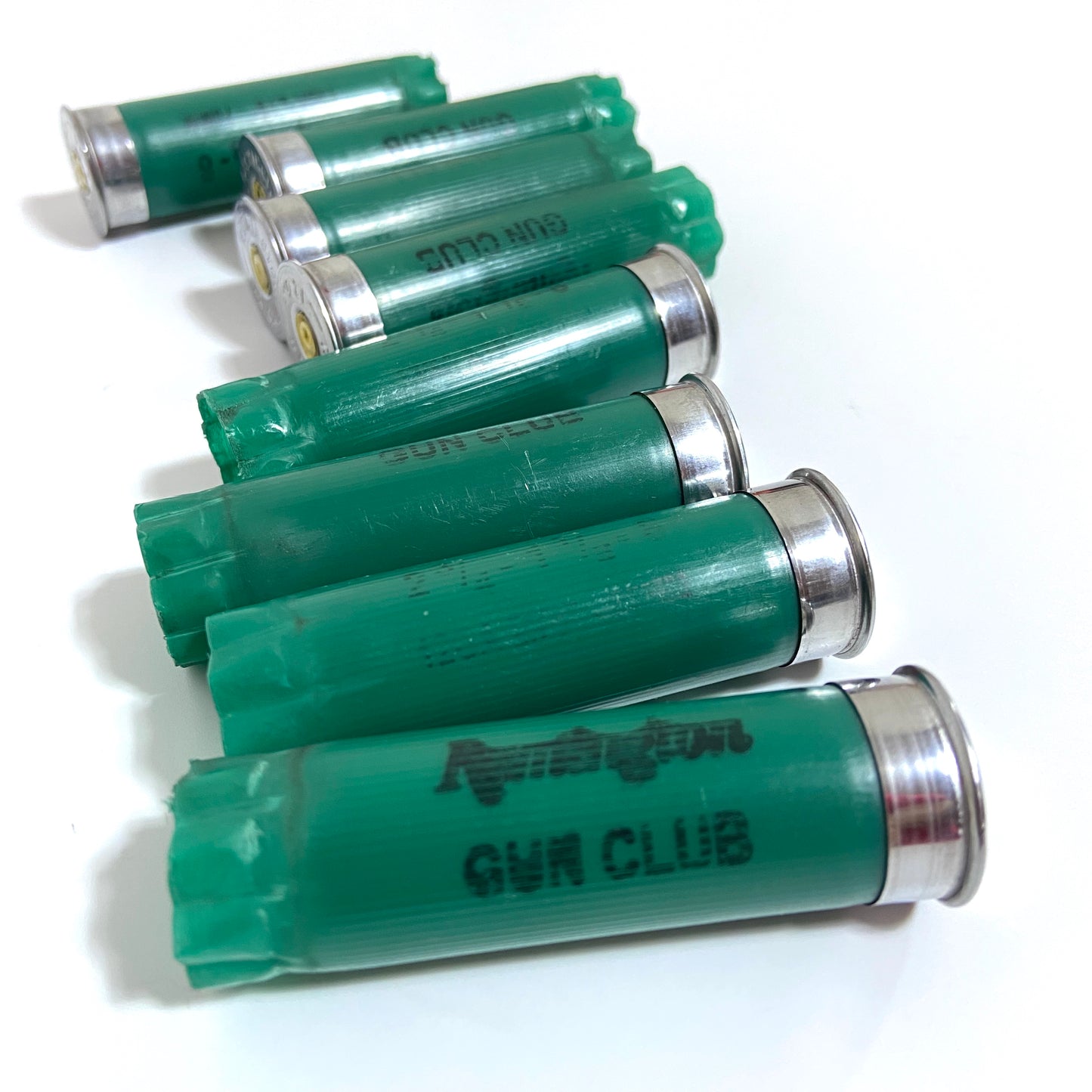 Seven spent green 12ga Remington Gun Club cartridges arranged diagonally with GUN CLUB text visible