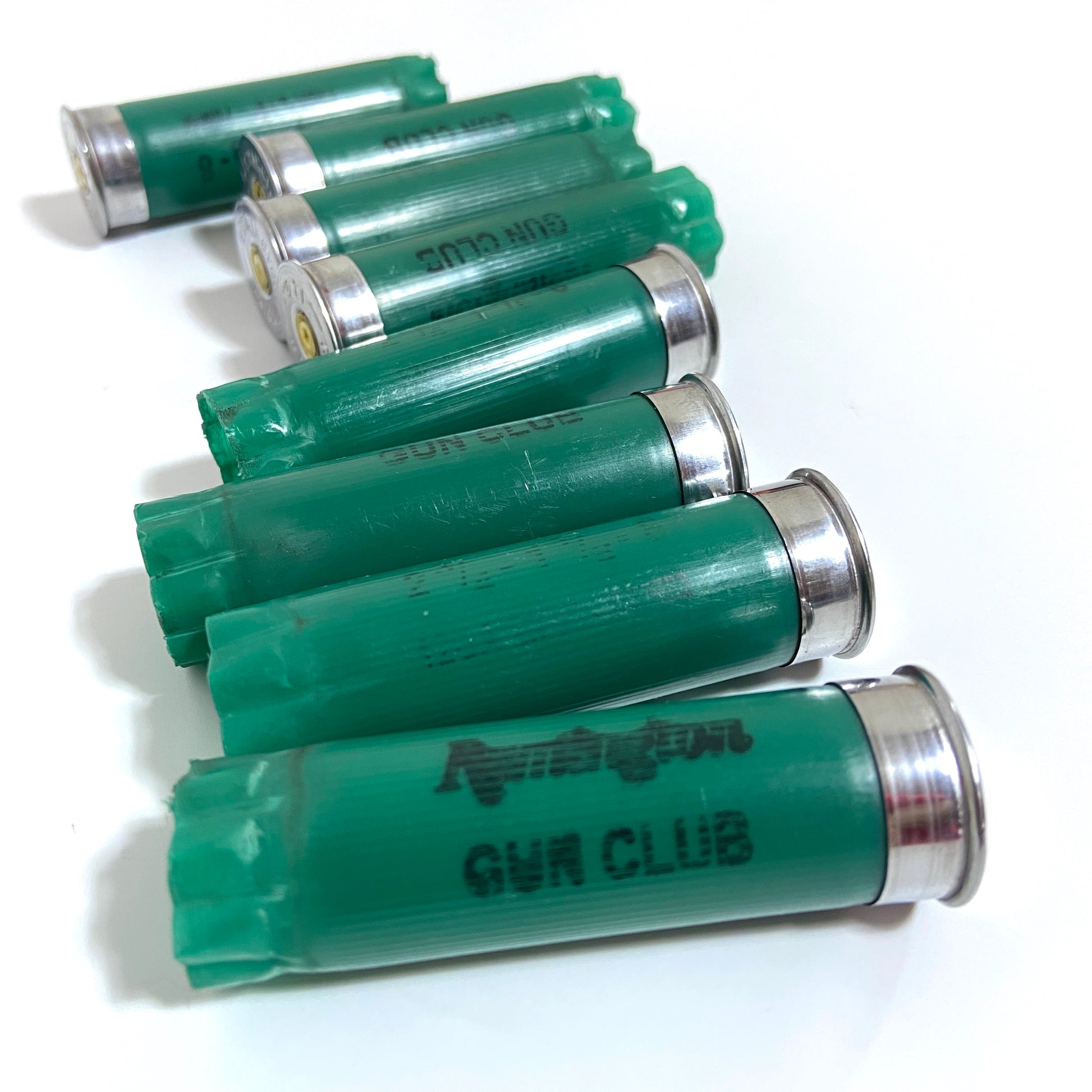 Seven spent green 12ga Remington Gun Club cartridges arranged diagonally with GUN CLUB text visible