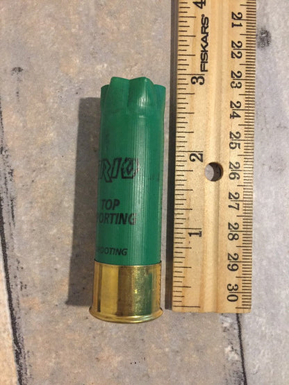 Single empty green 12 gauge RIO Top Sporting shotgun shell with brass base next to a wooden ruler showing approximately 2.75 inches in length