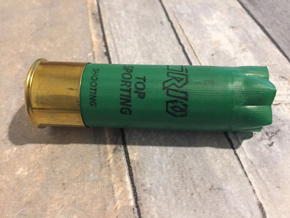 Single empty green 12 gauge RIO Top Sporting shotgun shell with brass base on a wood deck
