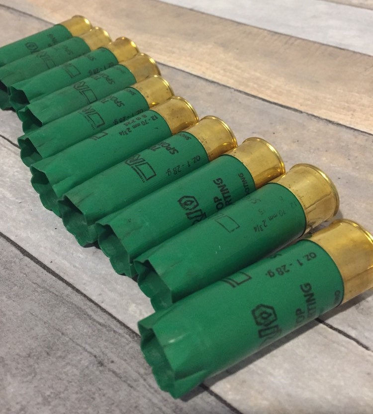 Row of empty green 12 gauge RIO Top Sporting shotgun shells with brass bases lying on a wood deck