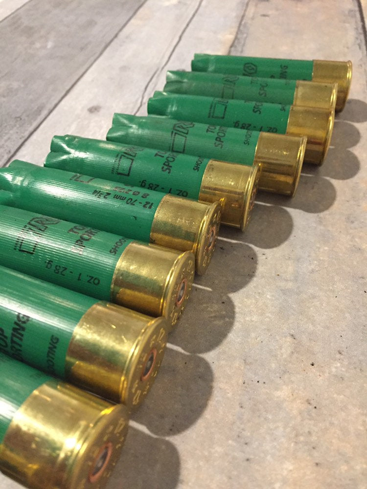 Row of empty green 12 gauge RIO Top Sporting shotgun shells with brass bases on a concrete surface