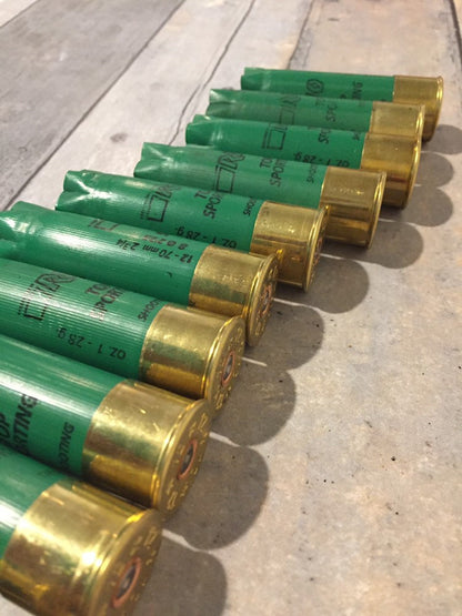 Row of empty green 12 gauge RIO Top Sporting shotgun shells with brass bases on a concrete surface